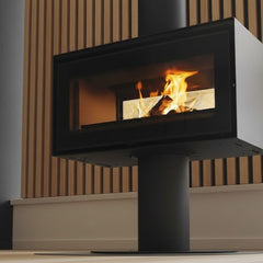 Modern freestanding fireplace with flames inside, set against a neutral wall.